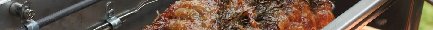 Arrosto di maiale su girarrosto in acciaio inox con erbe aromatiche, perfetto per barbecue all'aperto.