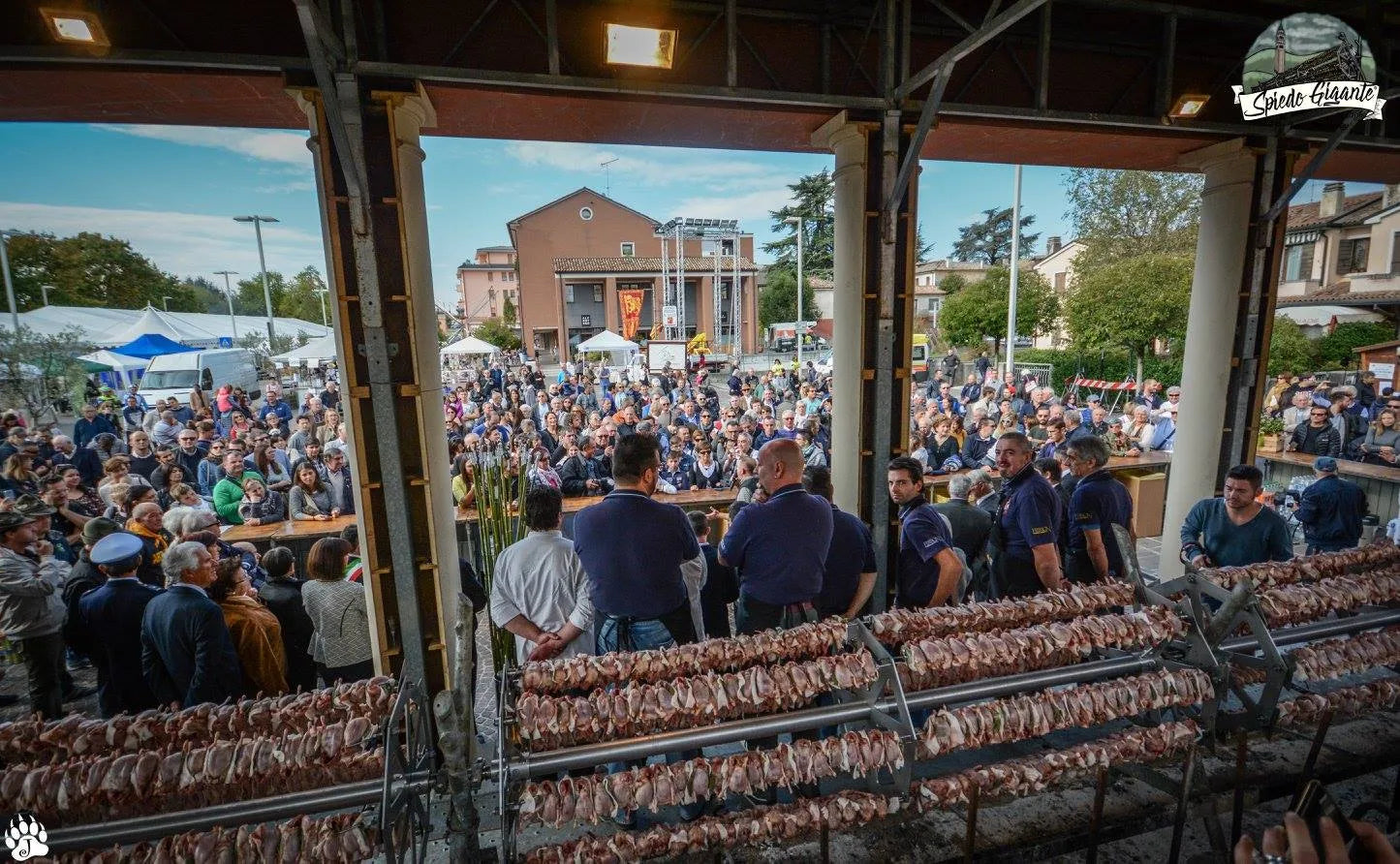 Spiedo gigante con carne in cottura davanti a folla, evento all'aperto con barbecue professionale