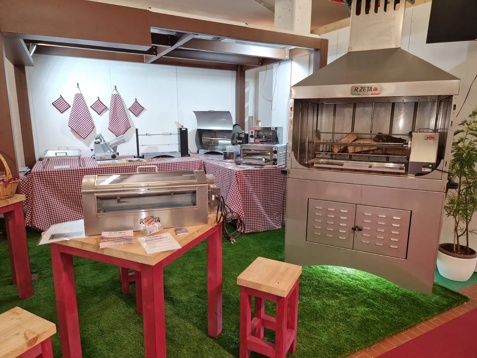 Barbecue e girarrosto in acciaio inox per cucina professionale e privata, esposti su tavoli con tovaglia a quadri