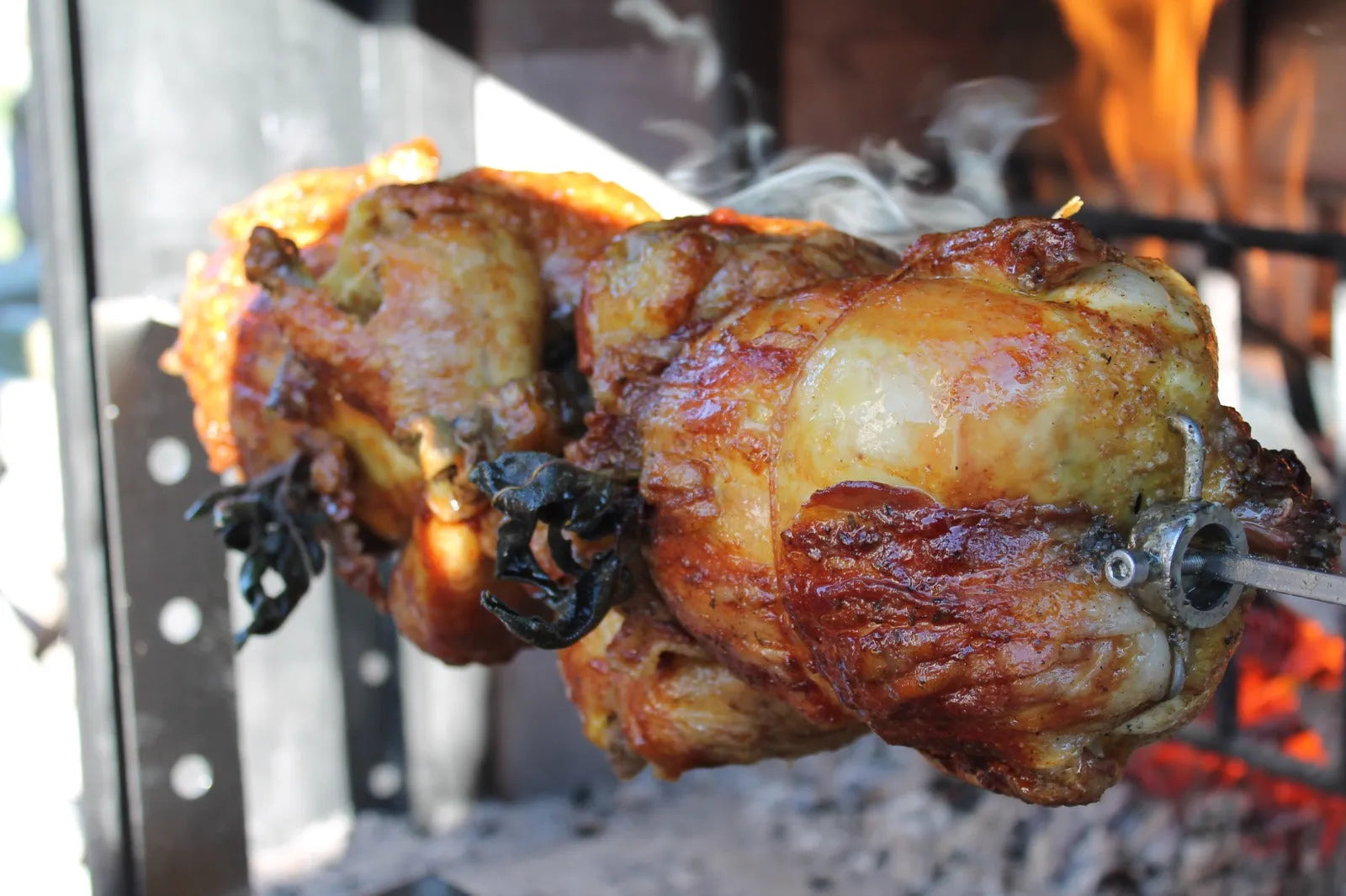Polli arrosto su girarrosto in acciaio inox con fiamme e fumo, ideale per barbecue all'aperto