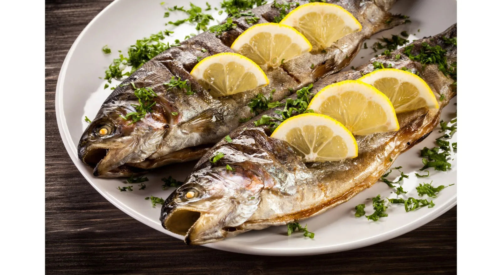 Pesce grigliato con fette di limone e prezzemolo su piatto bianco