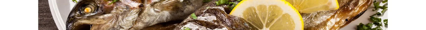 Pesce grigliato con fette di limone e prezzemolo su piatto bianco