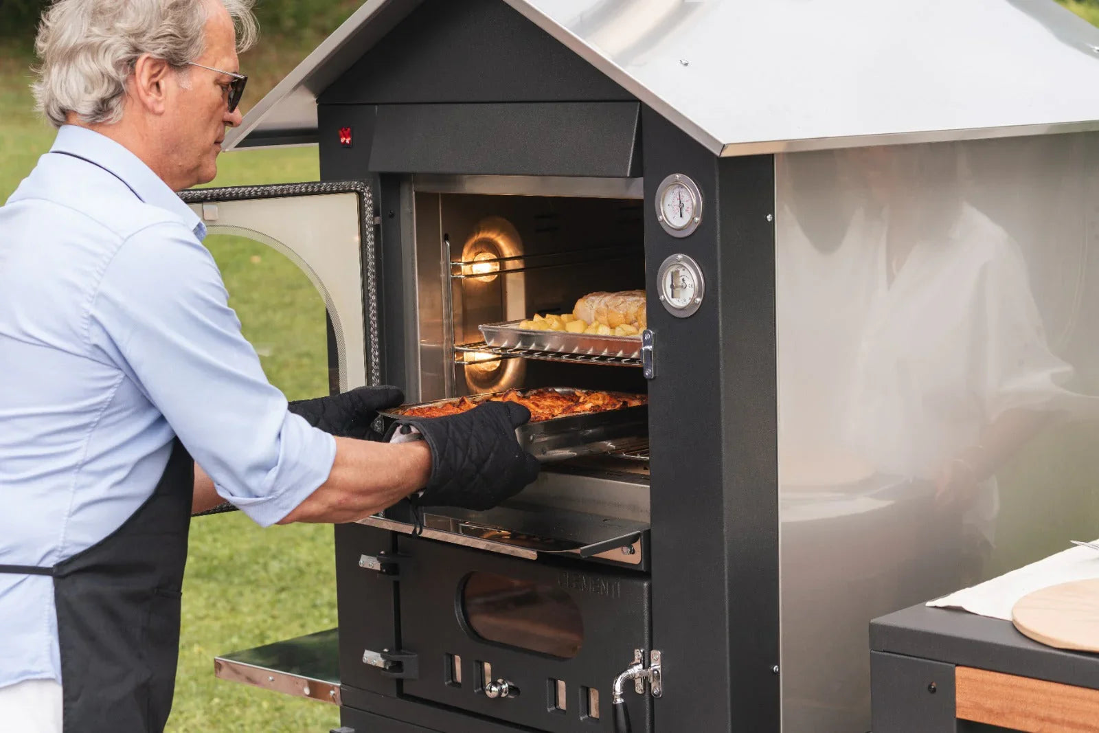 Uomo che cuoce cibo in un barbecue professionale in acciaio inox all'aperto