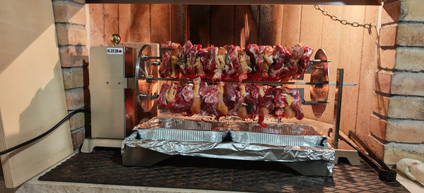 Girarrosto in acciaio inox con carne e pollo su spiedi, pronto per barbecue all'aperto.