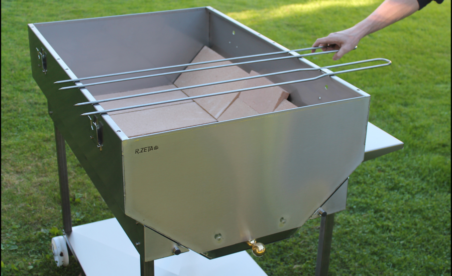 Girarrosto in acciaio inox RZeta con griglia regolabile, ideale per barbecue all'aperto su erba.