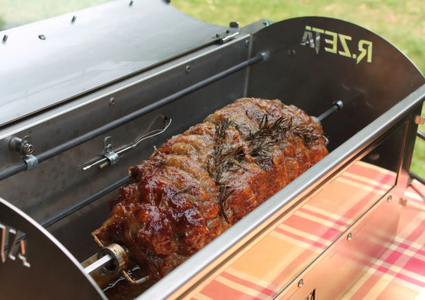 Arrosto di maiale su girarrosto in acciaio inox con rosmarino, pronto per barbecue all'aperto.